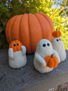 three stuffed ghost dolls sitting on top of a stone wall next to a large pumpkin