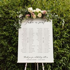 a white sign with flowers on it sitting in front of some green plants and bushes