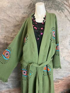 41023 Evil Eye Kimono Robe. How fun are these!!! We have more colors and prints coming soon. This olive-hued, handmade kimono-style robe is crafted from 100% organic cotton, and emblazoned with an all-seeing evil eye motif. With its gender-neutral design, it's a versatile, protective cover-up for the beach, the spa, festivals, or any time you want to bring a casual look to the next level. It's believed that the evil eye will keep wearers safe from negative energy and carry luck in other areas of Cotton Kimono For Fall Loungewear, Cotton Kimono For Loungewear In Fall, Cotton Open Front Kimono For Fall, Fall Cotton Open Front Kimono, Cotton Robe With Kimono Sleeves For Fall, Oversized Cotton Bohemian Kimono, Oversized Cotton Kimono With Open Front, Oversized Cotton Open Front Kimono, Handmade Long Sleeve Kimono For Summer