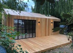 a small wooden building with lots of windows on the front and side of it, surrounded by greenery