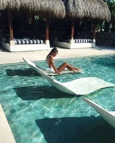 a woman is sitting on a surfboard in the middle of a pool with thatched umbrellas