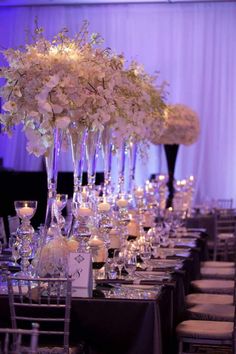 a long table is set with candles and flowers in tall vases on each side