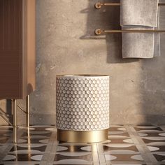 a white and gold trash can sitting on top of a tiled floor next to a towel rack