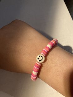 bracelet with different shades of pink beads, and a smiley face charm in the middle. Casual Pink Friendship Bracelets With Heart Beads, Casual Pink Beaded Bracelets With Heart Beads, Fun Pink Beaded Bracelets, Trendy Pink Beaded Bracelets With Heart Beads, Fun Pink Beaded Bracelets With Round Beads, Pink Colorful Beads Friendship Bracelets, Fun Pink Friendship Bracelets With Colorful Beads, Casual Pink Beaded Bracelet With Heart Beads, Pink Beaded Stretch Bracelet