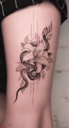 a woman's thigh with a flower tattoo on her lower leg and an snake crawling around the side