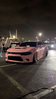 two pink cars parked in a parking lot at night with people standing around the car