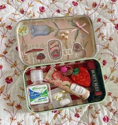 an open tin with various items in it sitting on a floral print bed spread,