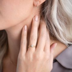 a woman with blonde hair wearing a yellow gold ring and diamond band, looking down at her left hand