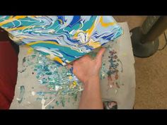 someone is painting on a piece of paper with blue, yellow and white swirls