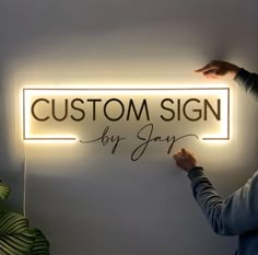 two people holding up a lighted sign that says custom by jayy on the wall