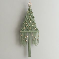 a green christmas tree ornament hanging on a wall with white balls and tassels