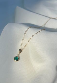 a gold necklace with a green stone on it sitting on top of a white cloth