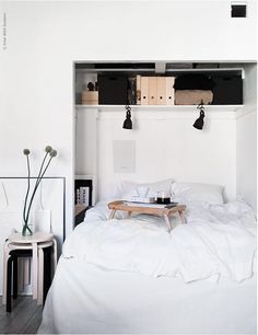 a bed with white sheets and pillows in a small room next to a shelf filled with books