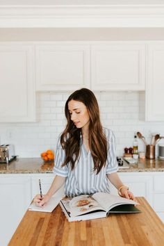 a woman sitting at a kitchen table with an open book