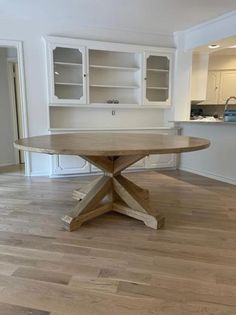 an empty kitchen with wooden floors and white cabinets in the background, there is a round dining table