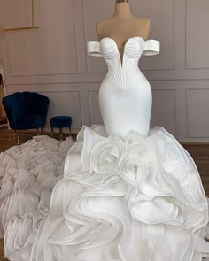 a white wedding dress on display in a room with blue chairs and other items around it