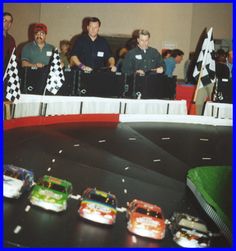 some people and cars on a track at a toy car race event with flags in the background