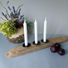 three white candles sitting on top of a wooden board next to plums and flowers