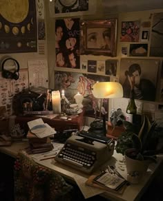 a cluttered desk with an old typewriter, lamp and pictures on the wall