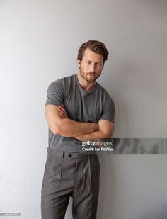 a man standing with his arms crossed in front of a white wall and looking at the camera