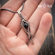 a hand holding a wire wrapped pendant with an eye in it's center, on a wooden table