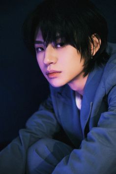 a young man with black hair and blue eyes is posing for the camera in a dark room