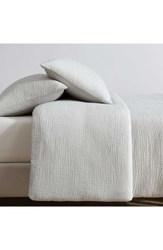 two white pillows on top of a bed with linens in the sheets and pillow cases