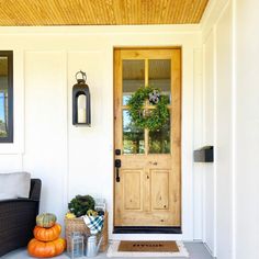 the front door is decorated with pumpkins and greenery for fall time, along with an entry mat