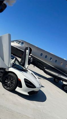 a white sports car parked next to an airplane on the tarmac with its door open