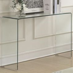 a glass console table with flowers and books on the shelf next to it in front of a white wall