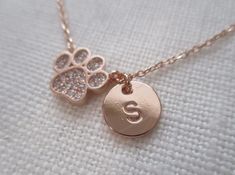 a dog paw and initial charm necklace on a white cloth with the letter s in it