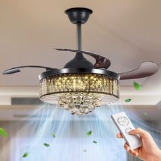 a person holding a remote control in front of a ceiling fan with lights on it