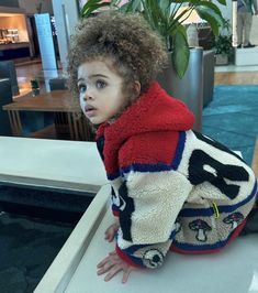 a young child sitting on top of a counter next to a plant in a living room