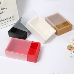 three different colored boxes sitting next to each other on a white table with an envelope in the background