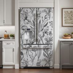 the refrigerator is decorated with floral wallpaper and white cabinets, along with wooden flooring