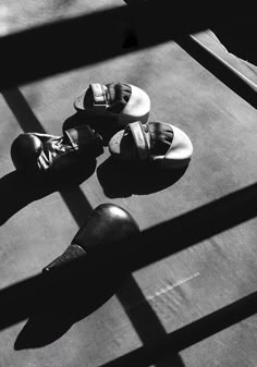 black and white photograph of three pairs of shoes on the ground with shadows from them