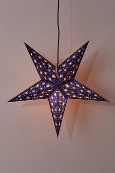 an origami star hanging from a string on the wall with lights around it