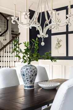 a blue and white dining room with chandelier, plates and flowers on the table