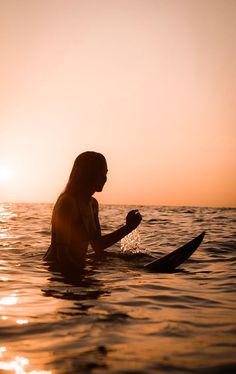 a woman sitting on a surfboard in the ocean at sunset or dawn, holding her hand out