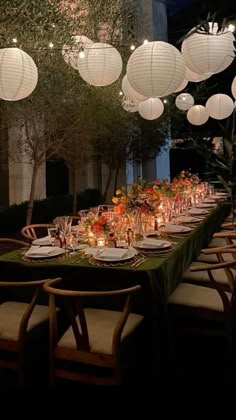 a long table with paper lanterns hanging from it's ceiling and place settings on the tables