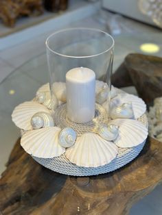 a glass candle holder with seashells and a white candle sitting on top of it