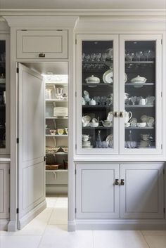 a kitchen with white cabinets and dishes on the glass front doors, in an open area