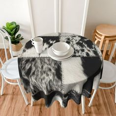 the table is set with two cups and saucers on it, along with a black and white cow - print tablecloth