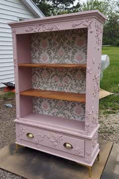 an old dresser painted pink with floral wallpaper and gold hardware on the bottom shelf