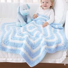 a baby sitting in a crib with a blue and white blanket on top of it