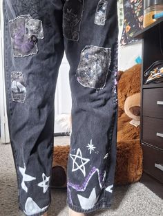 a person standing in front of a teddy bear wearing jeans with patches and stars on them