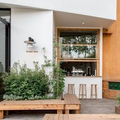 the outside of a restaurant with wooden benches and plants on the side wall, along with potted plants