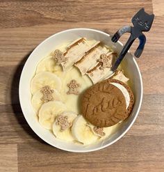 a bowl filled with bananas and peanut butter on top of a wooden table next to a pair of tongs