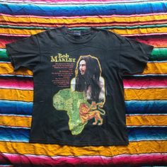 a black bob marley t - shirt sitting on top of a colorful blanket