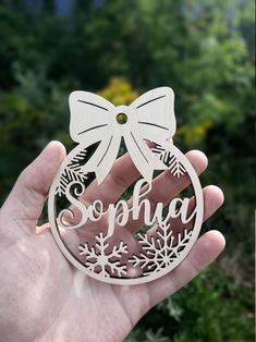 a hand holding a wooden ornament with snowflakes and a bow on it